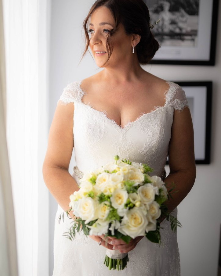 Bride holding a white rose bouquet by a window